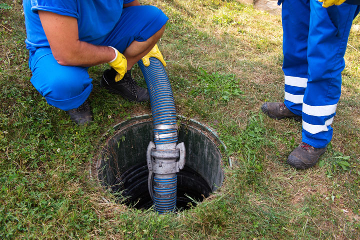 Deux ouvriers en maintenance d'une fosse septique à l'aide d'un tuyau de vidange